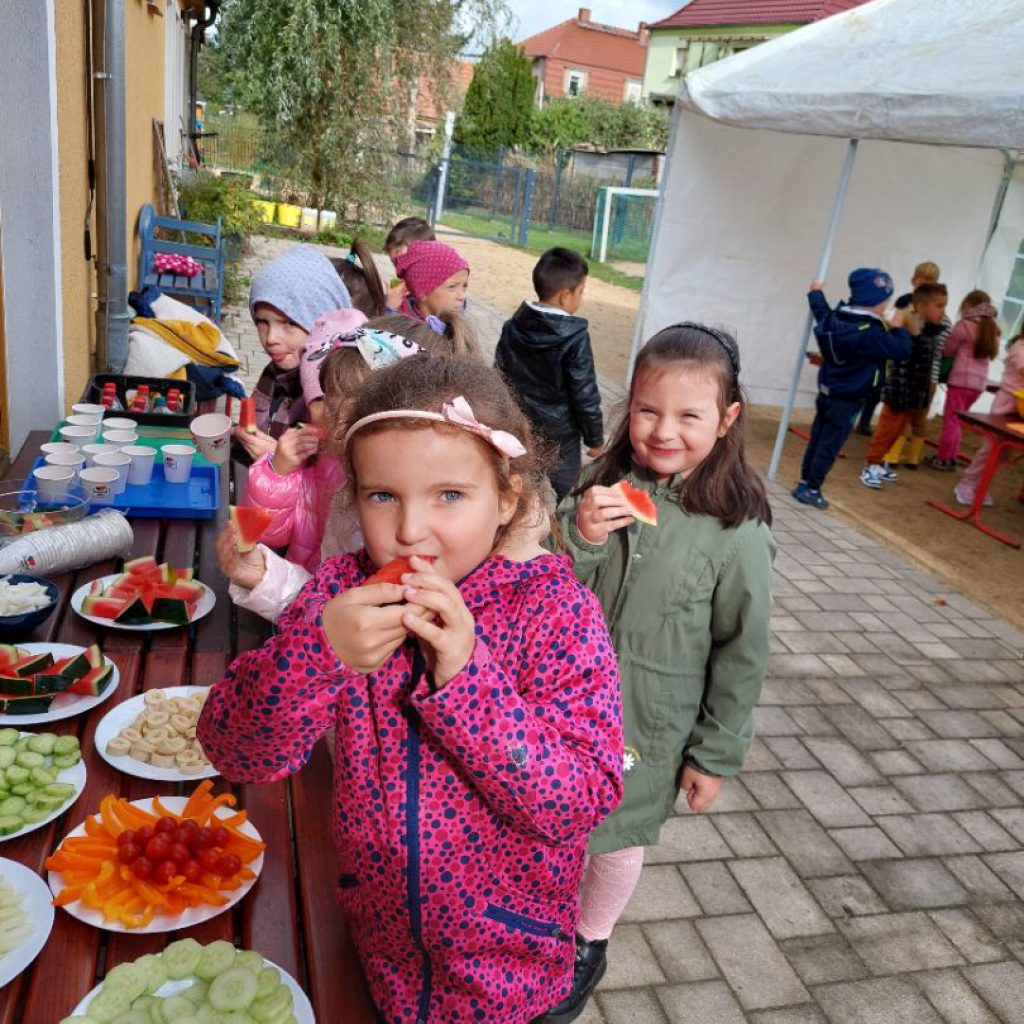 Dzieci częstują się warzywami i owocami z papierowych talerzy znajdujących się na stole.