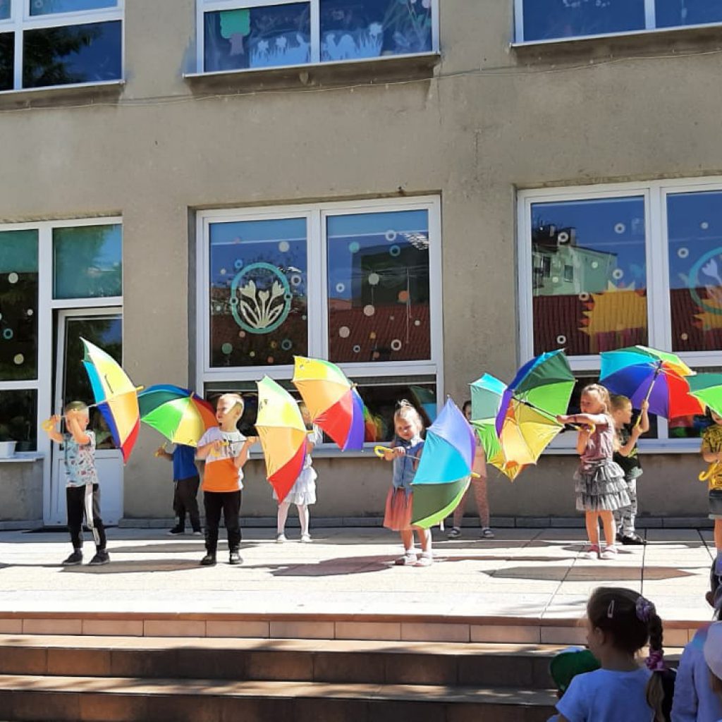 Dzieci przed przedszkolem tańczą z parasolkami