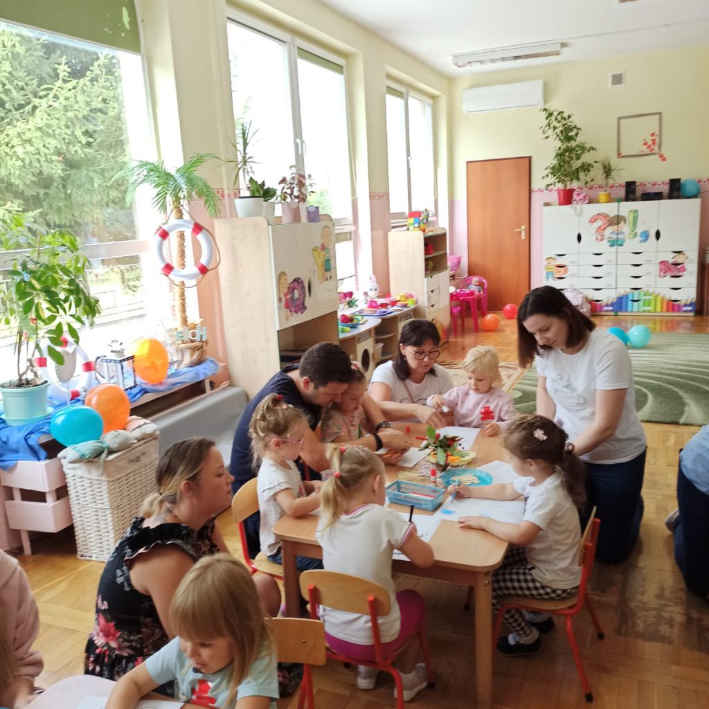 Rodzice z dziećmi rysują przy stolikach.