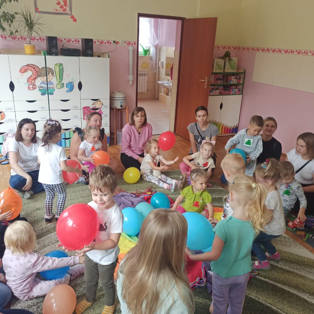 Rodzice i dzieci bawią się na dywanie z balonami.