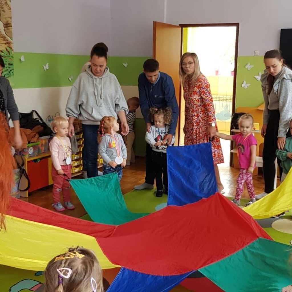 Rodzice z dziećmi bawią się z chustą animacyjną.