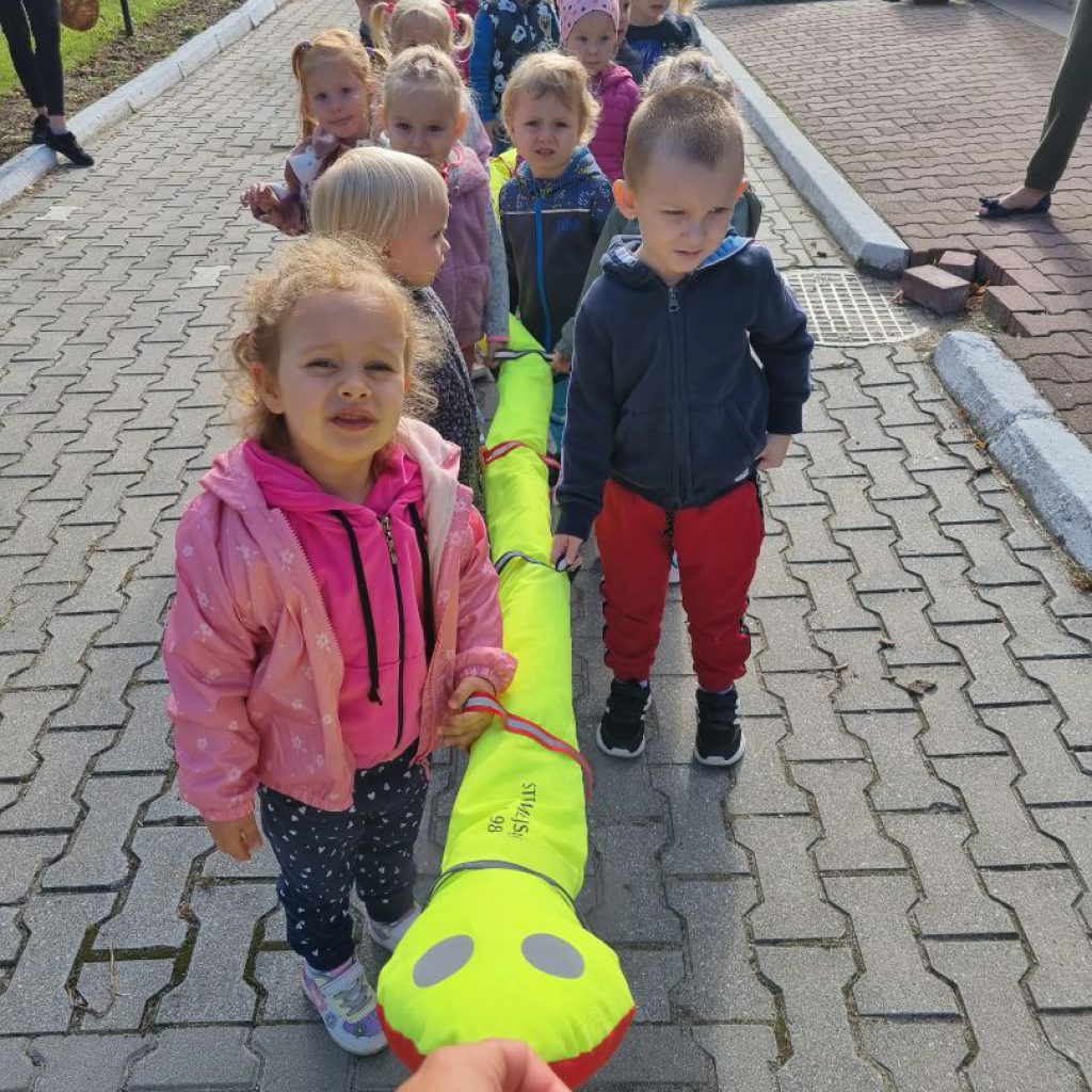 Grupa dzieci porusza się po drodze trzymając pomocniczego węża.