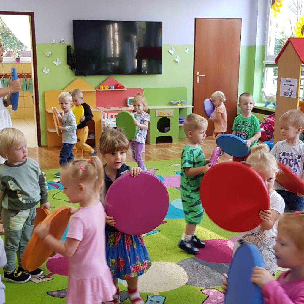Grupa dzieci porusza się po sali trzymając w rękach kolorowe kółka.