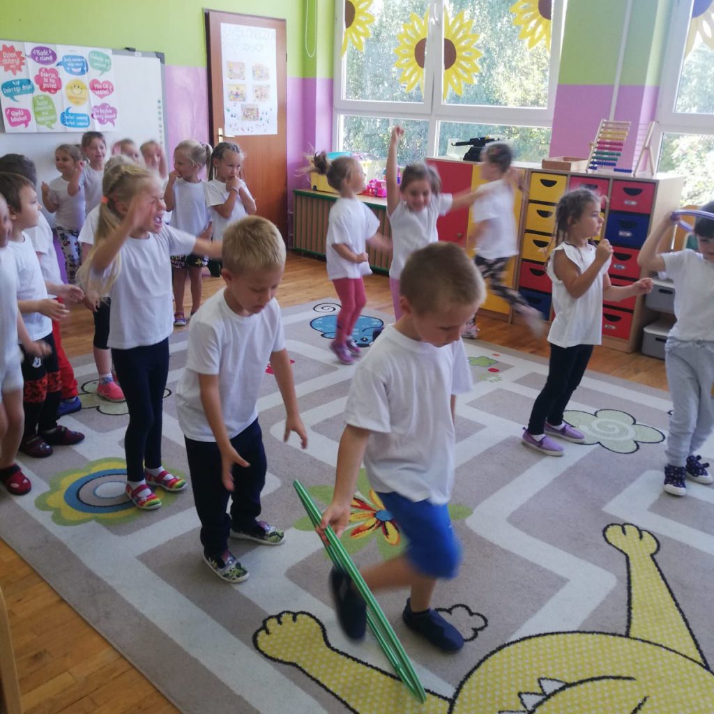 Dzieci ubrane w białe koszulki wykonują ćwiczenia gimnastyczne.