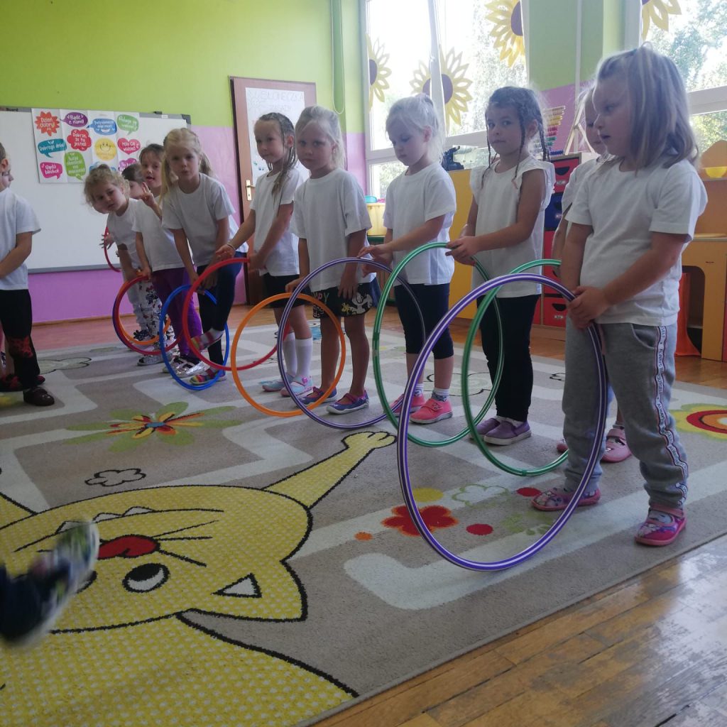 Dzieci ubrane w białe koszulki bawią się hulaj - hop na sali.