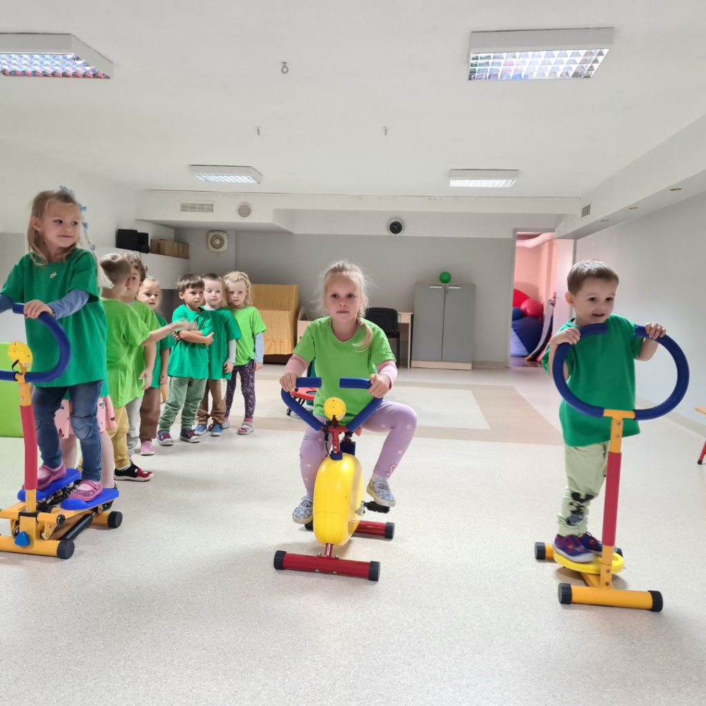 troje dzieci na pierwszym planie ćwiczy na sprzęcie sportowycm, pozostałe czekają w kolejce