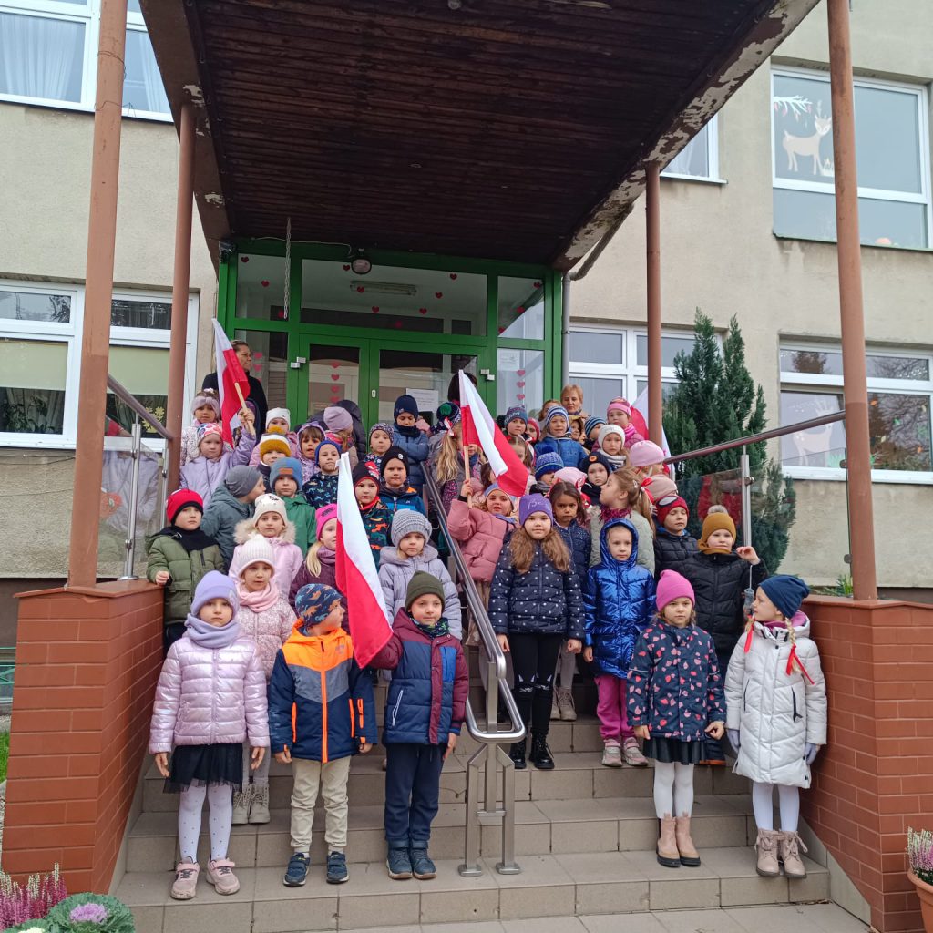 dzieci z flagami polski stoja na schodach przed przedszkolem