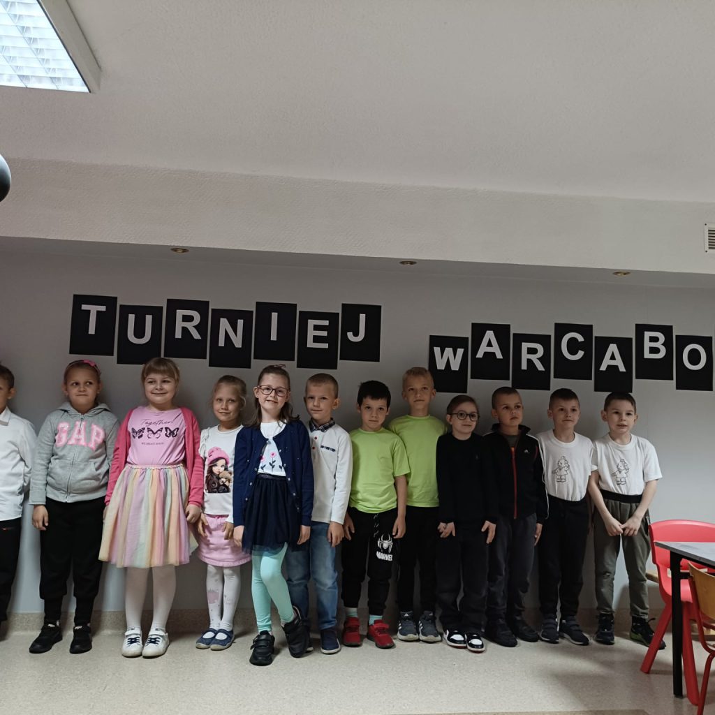 grupa dzieci pozuje na tle napisu turniej warcabowy