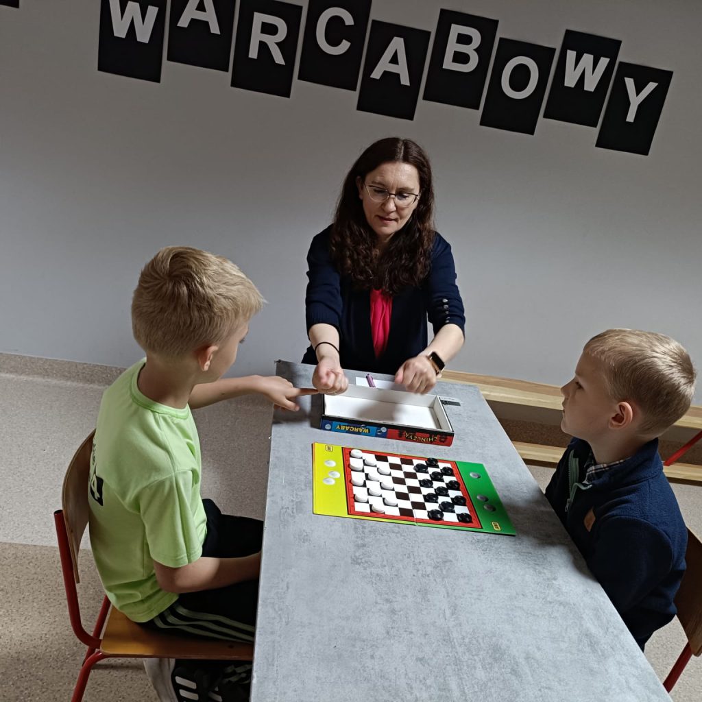 dwoje dzieci i dorosły grają w warcaby