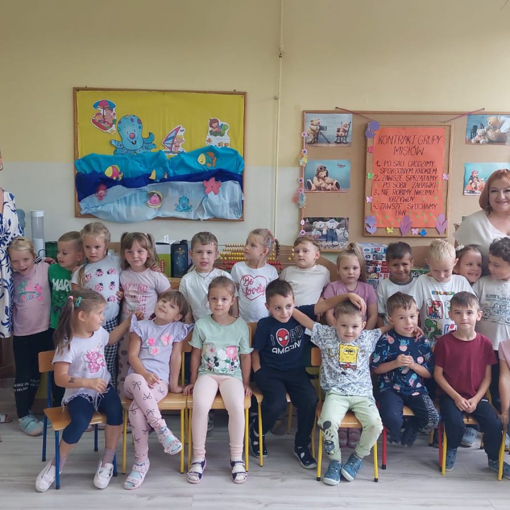 Grupa dzieci pozuje wraz z Paniami na tle tablicy
