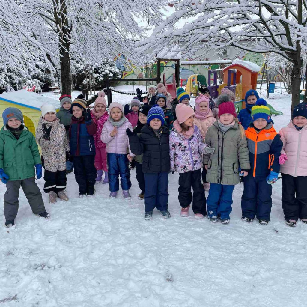 grupa dzieci pozuje na placu zabaw w zimowej scenerii