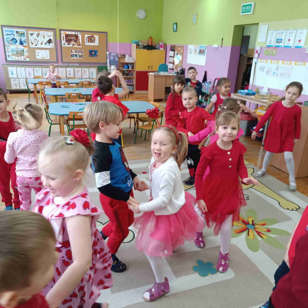 Grupa dzieci ubranych na biało i czerwono tańczy na dywanie