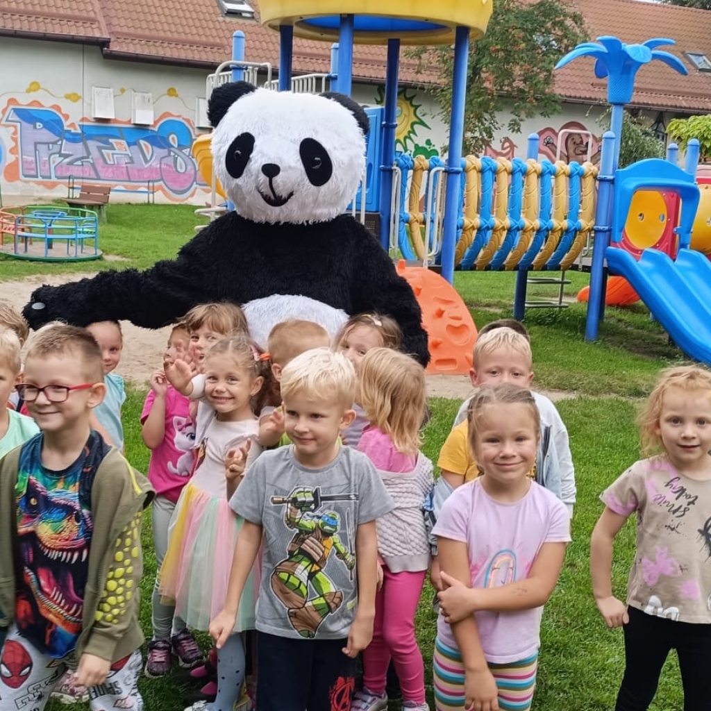 grupa dzieci pozuje z pandą na placu zabaw