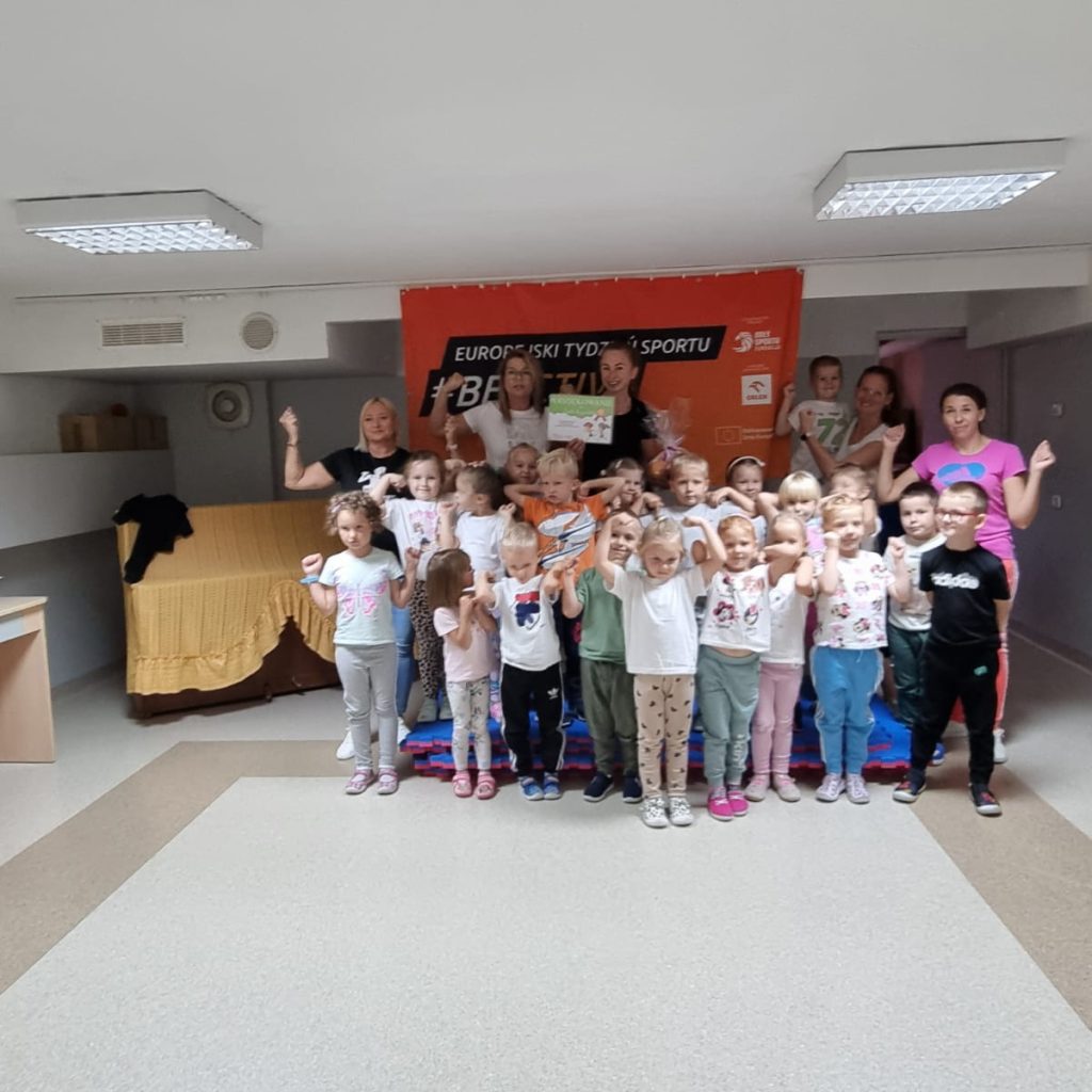 Dzieci pozują wraz z trenerką, rodzicami i Panią dyrektor na tle banera #beactive