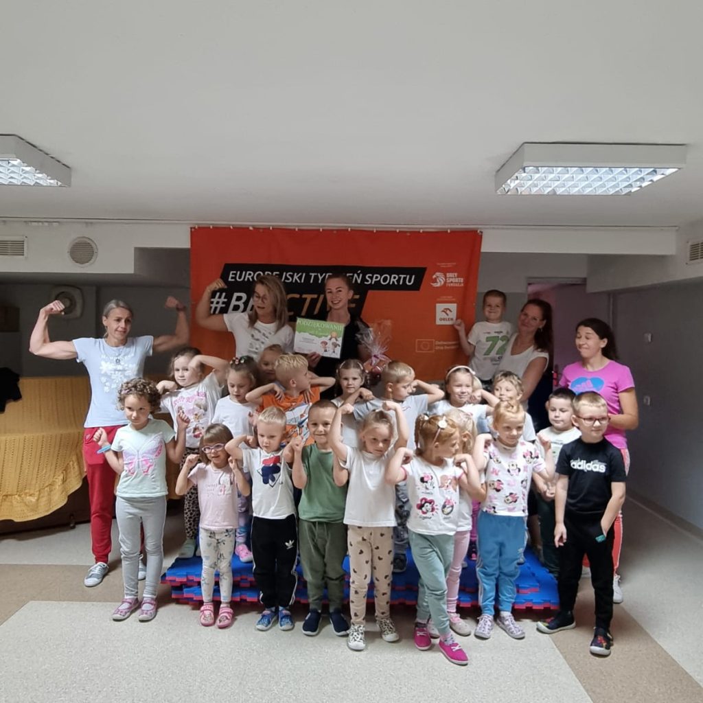 dzieci pozują z panią trenerką, opiekunami i rodzicami na tle banera #beactive