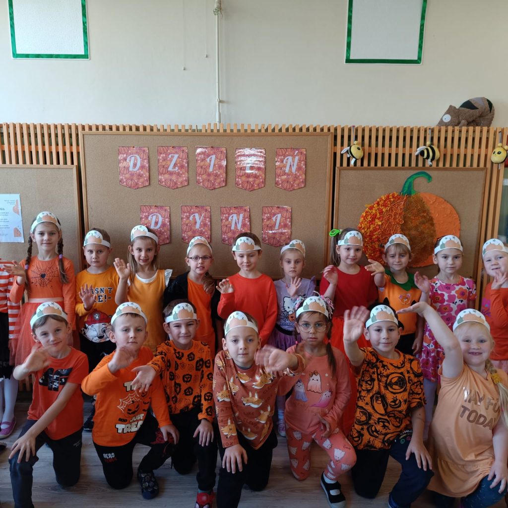 grupa dzieci ubranych na pomarańczowo w opaskach z dynia na głowie pozuje do grupowego zdjęcia