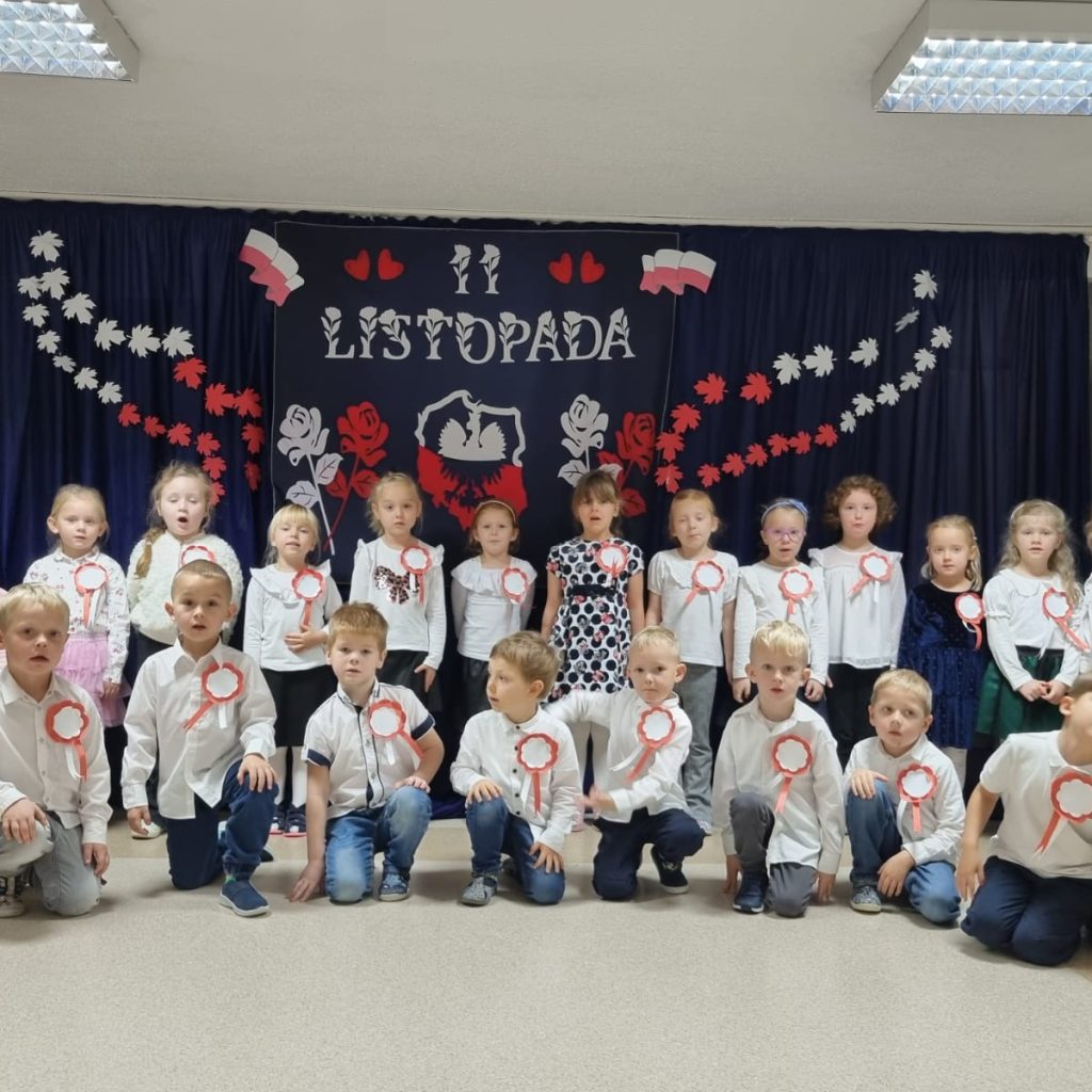 grupa Motylków pozuje w biało czerwonych strojach na tle napisu 11 listopada