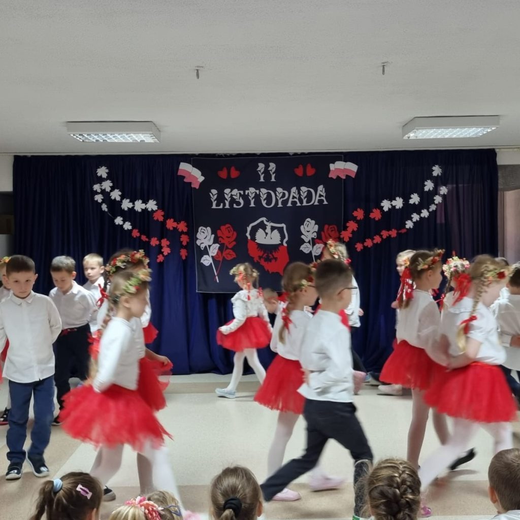 dzieci w białoczerwonych strojach tańczą Krakowiaka