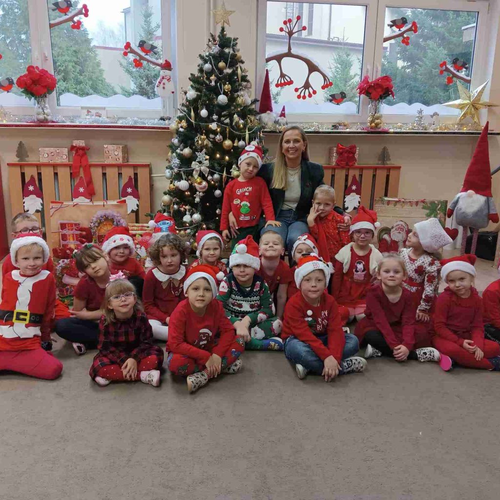 Grupa dzieci pozuje z mamą jednego z dzieci na tle choinki