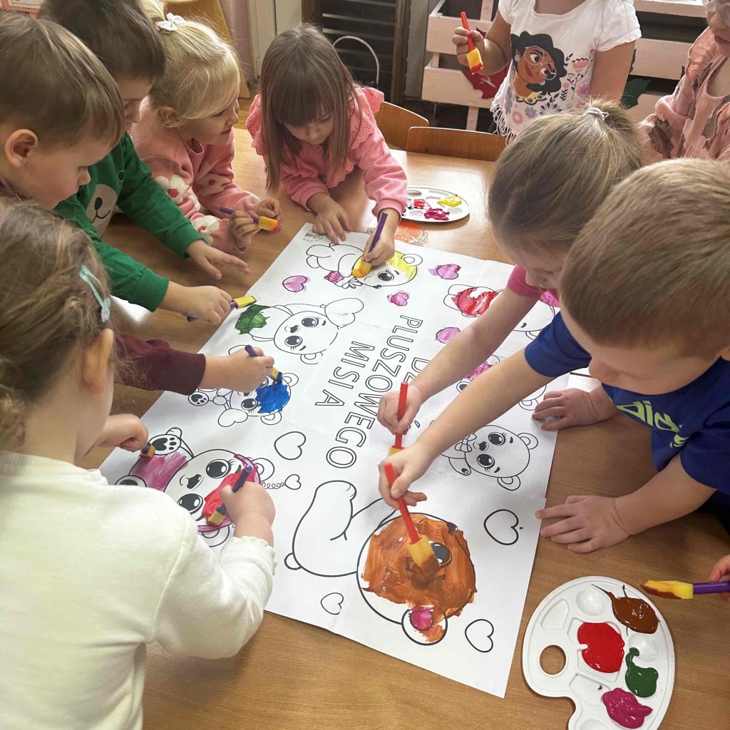 grupa dzieci maluje farbami plakat związany z dniem pluszowego misia