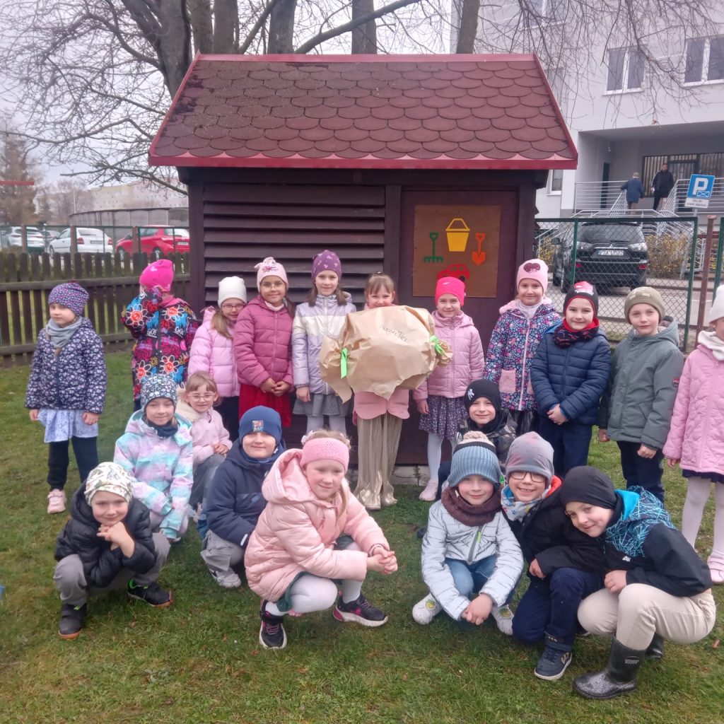 dzieci pozują z prezentem na tle szopki na zabawki ogrodowe